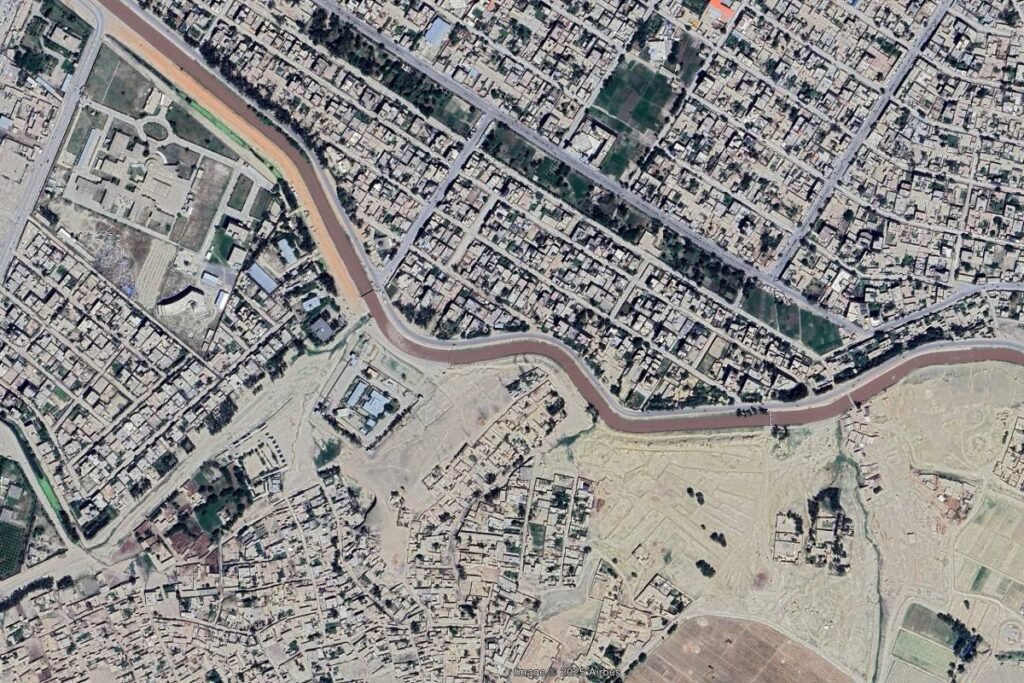 Aerial view of Jalalabad, Afghanistan, showcasing a winding river separating formal urban areas from informal settlements and open land.