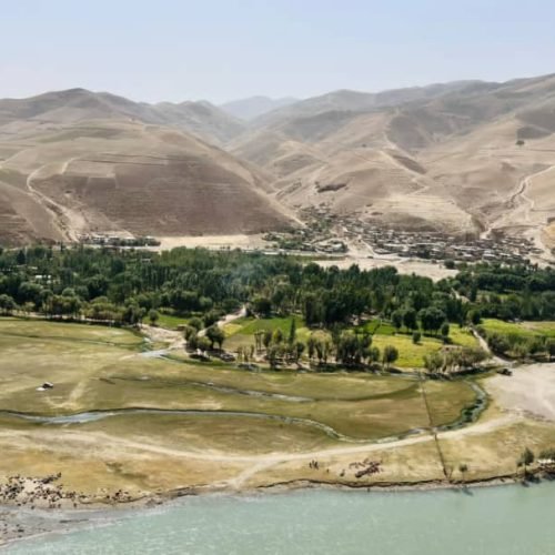 WhatsApp Bild 2024 10 15 um 07.10.28 675e212b A serene valley landscape in Afghanistan, featuring a lush green area bordered by a river and surrounded by arid mountains under a clear sky