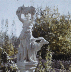 A white marble statue of a woman with a goat, surrounded by vibrant garden foliage, representing the elegance of 1920s Afghanistan