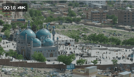 Aerial view of Karte Sakhi Shrine in Kabul, Afghanistan, featuring blue domes and minarets, surrounded by a large courtyard with visitors and a cemetery in the background.