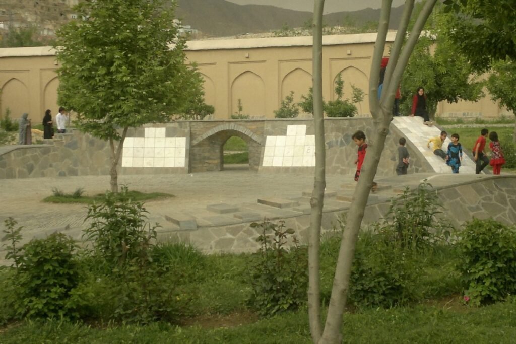 Adobe Express file 2 1 Newly built stone structure with an archway and white tile detailing, part of the modern additions by AKTC to Bagh-e Babur. Children play around the structure, with greenery and trees in the foreground.