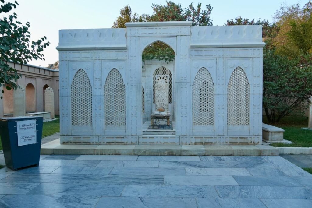 Adobe Express file 2 Babur's Tomb in Bagh-e Babur, surrounded by intricate white marble screens with arched patterns, situated within the lush garden