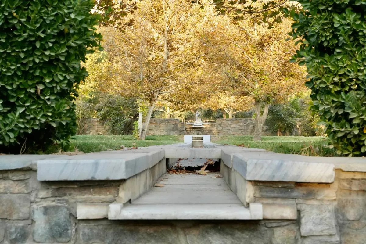 Central water channel at Bagh-e Babur, part of the Charbagh garden design, surrounded by lush greenery and trees with golden leaves, leading to a fountain in the distance.
