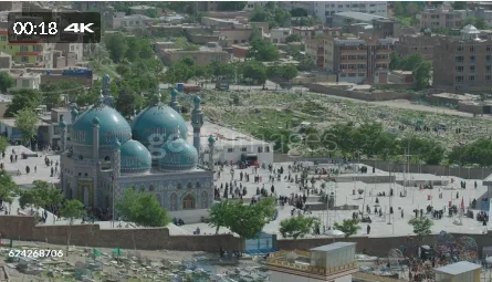 Aerial view of Karte Sakhi Shrine in Kabul, Afghanistan, featuring blue domes and minarets, surrounded by a large courtyard with visitors and a cemetery in the background.