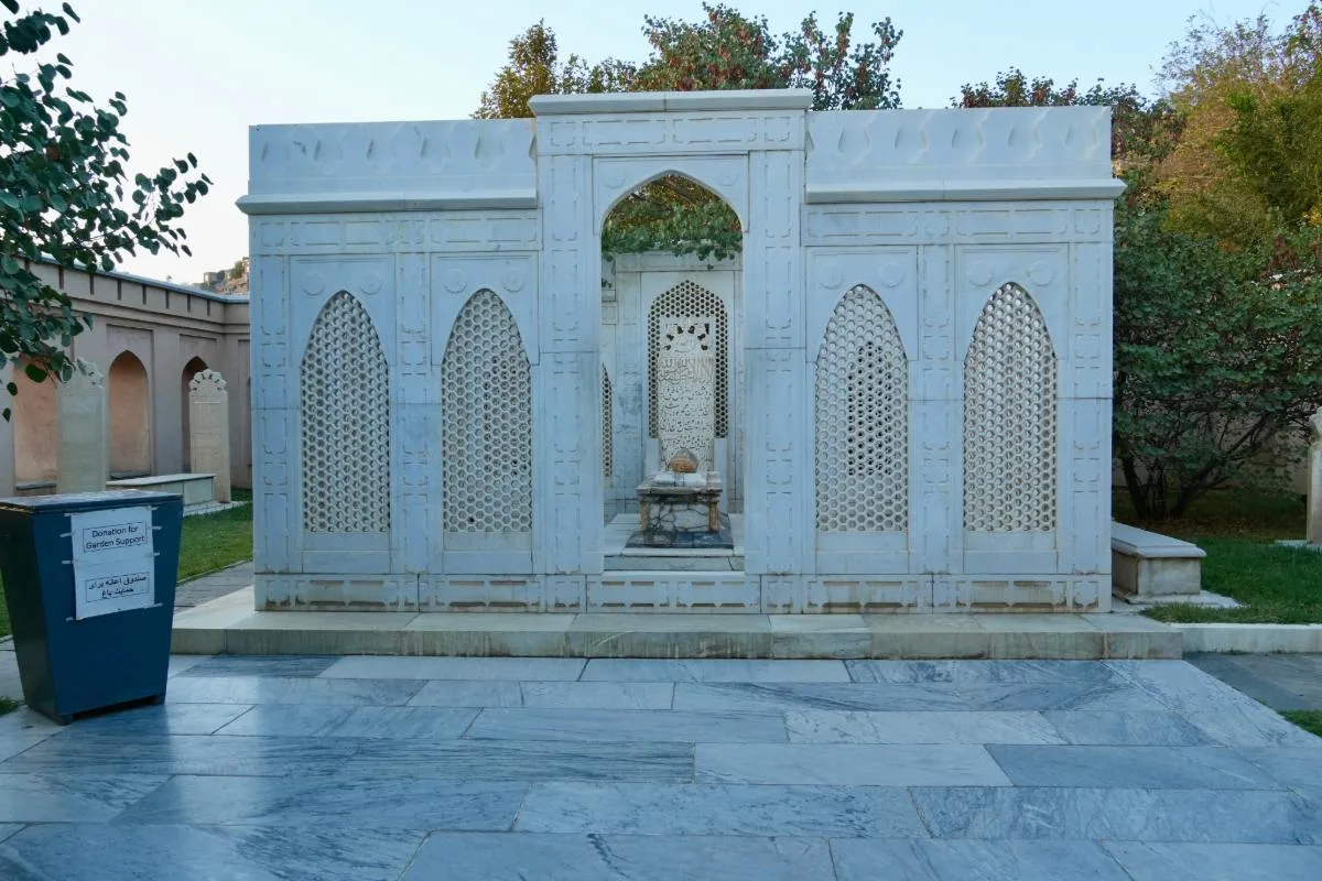 Babur's Tomb in Bagh-e Babur, surrounded by intricate white marble screens with arched patterns, situated within the lush garden