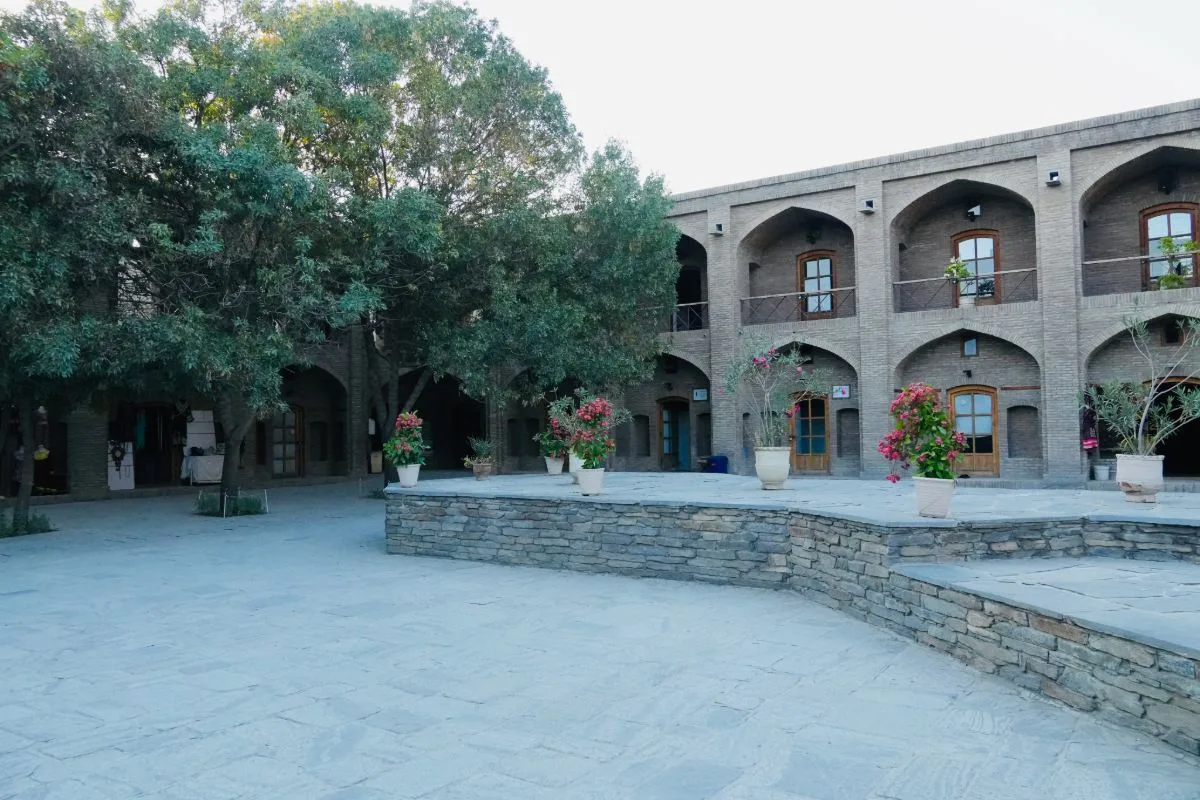 An inner courtyard in Bagh-e Babur, surrounded by arched brick structures, potted flowers, and large trees providing shade.