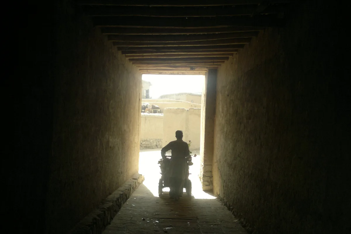 A person walking with a cart through a covered pathway in the historic district of Murad Khani, illuminated by light at the exit.