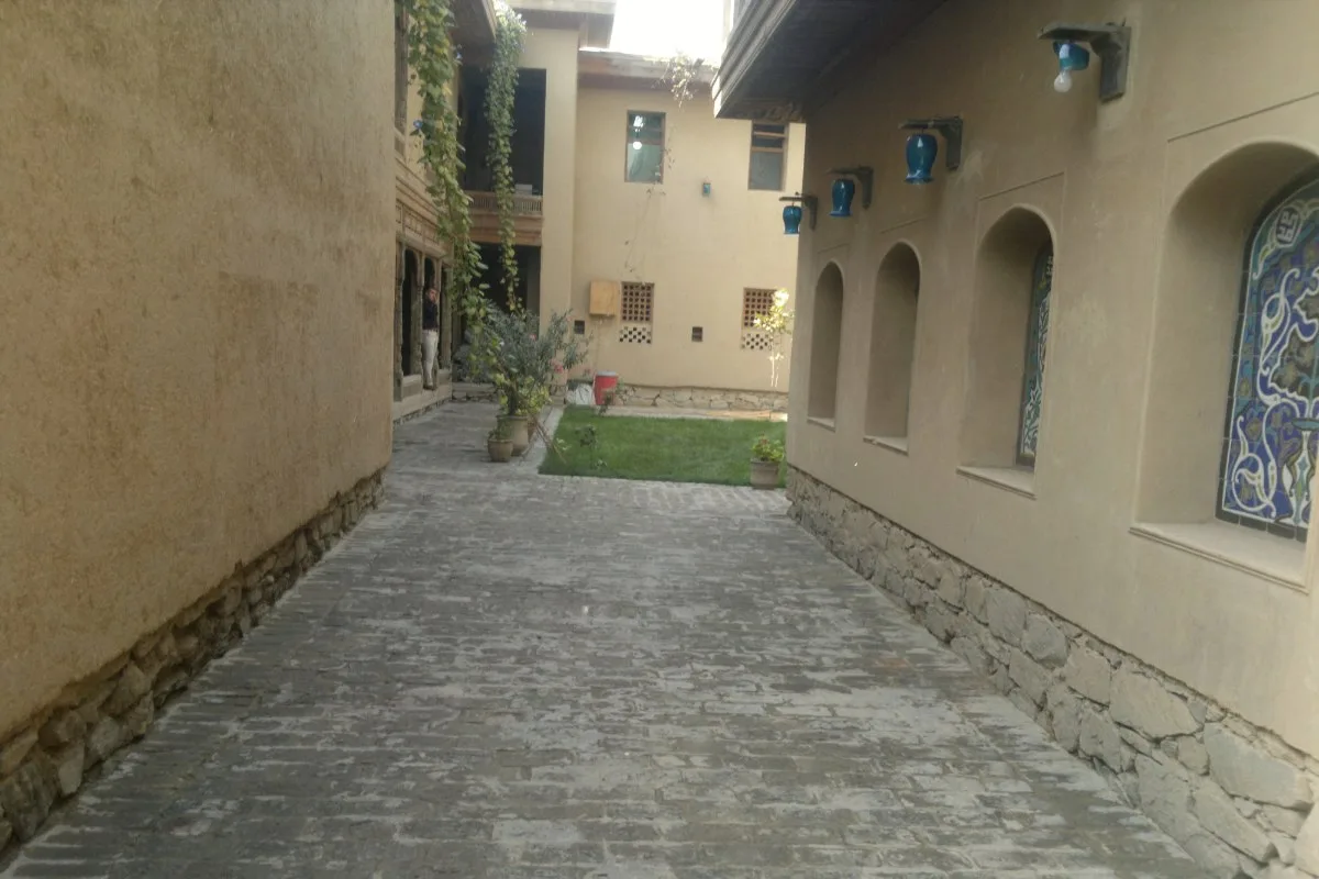 Pathway leading to a courtyard surrounded by traditional Afghan architecture, with blue lamps and stained glass windows adorning the walls.