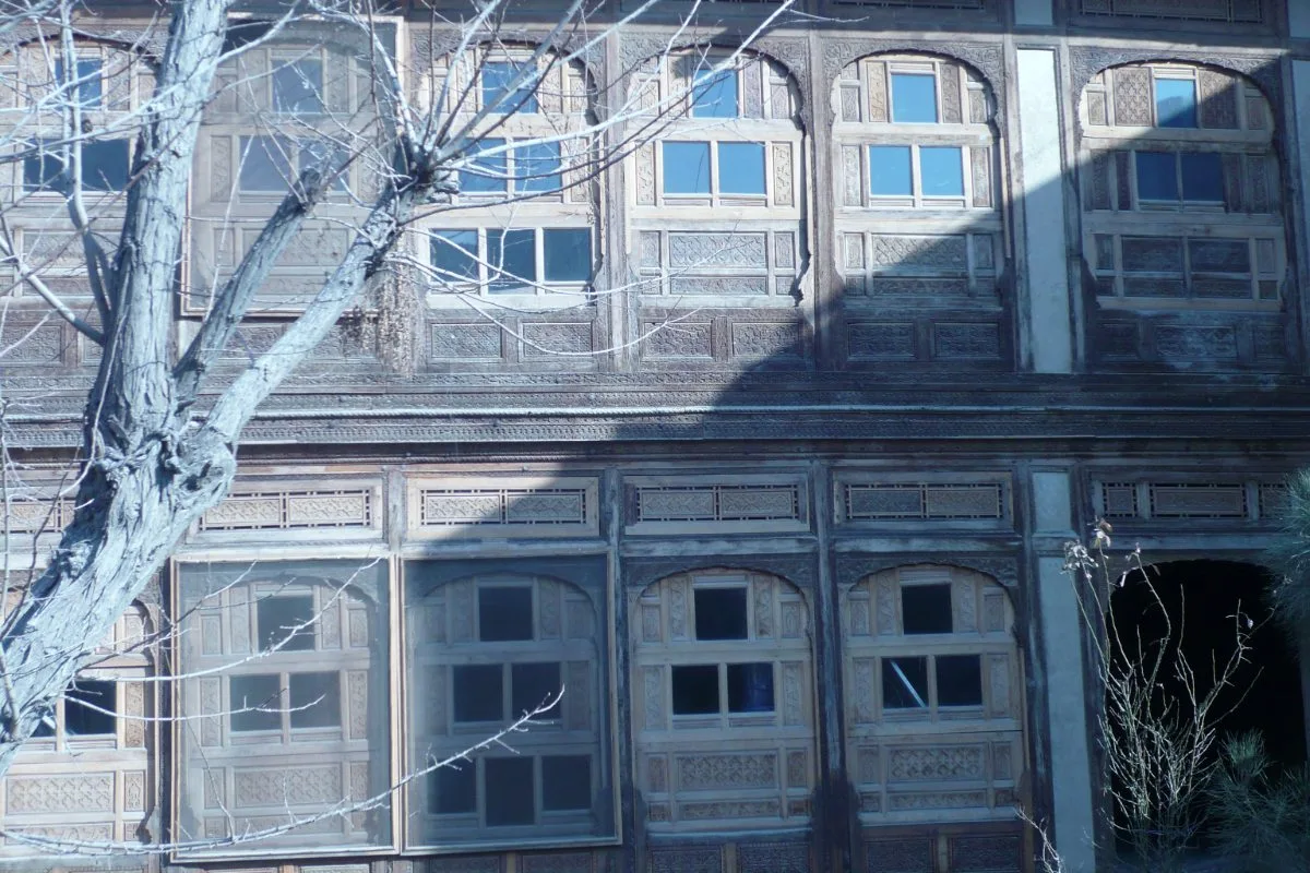 Detailed facade of a traditional wooden house in the old city of Kabul, showcasing intricate carvings and arched windows.