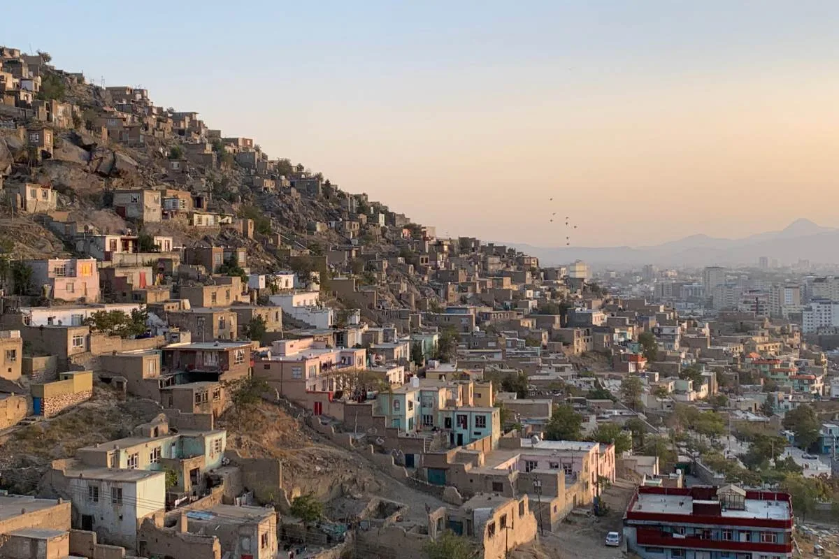 Kabul urban identity. View of a hillside informal settlement with closely packed houses extending across the slope, under a pastel-colored evening sky in Kabul
