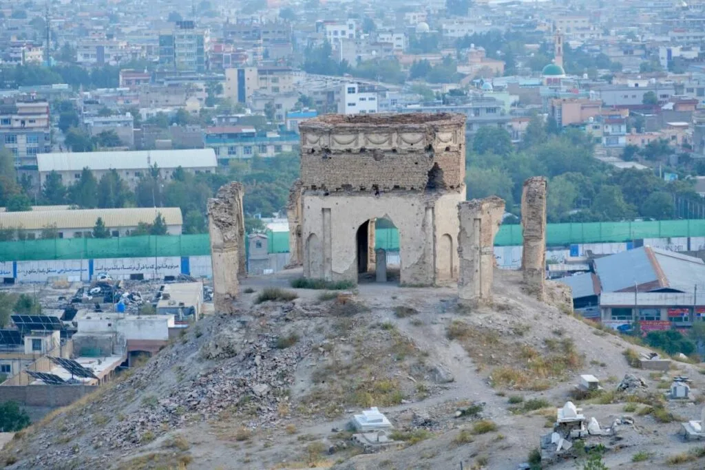 Ruined structure on a hilltop in Kabul, believed to be a remnant of the Mujahideen war, with a backdrop of urban buildings and greenery.