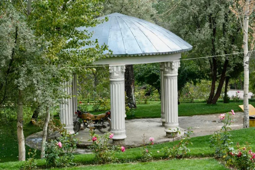 A small pavilion with ornate columns and a metal roof in Bala Bagh gardens, surrounded by lush greenery and blooming roses