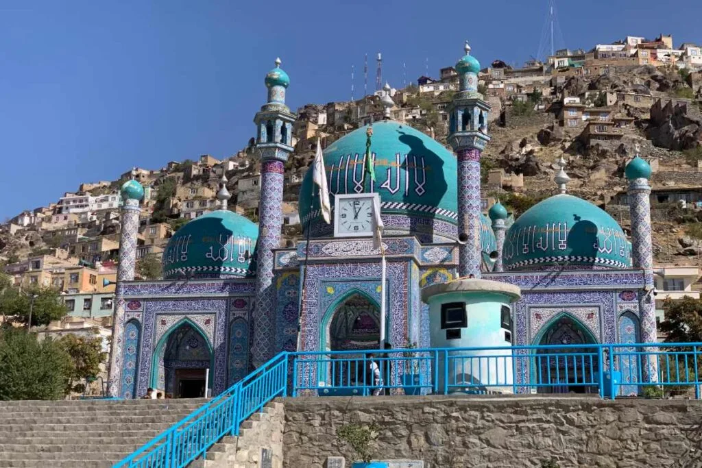 Front view of the Karte Sakhi Shrine in Kabul, showcasing its turquoise domes, intricate Islamic patterns, and surrounding hillside homes.